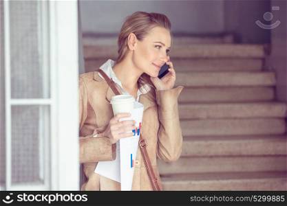 Portrait of a beautiful blond student girl talking on the phone and drinking coffee, using smart technology for work and communication, modern life of young people