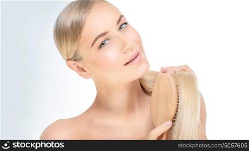 Portrait of a beautiful blond woman combing her perfect straight hair over clear background, fashion model wearing natural makeup