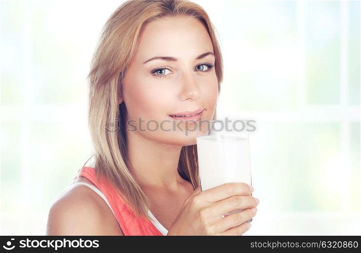 Portrait of a beautiful blond woman drinking milk at home, organic beverage for the breakfast, healthy nutrition concept