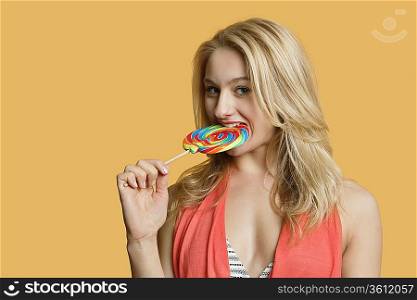 Portrait of a beautiful blond woman eating lollipop over colored background