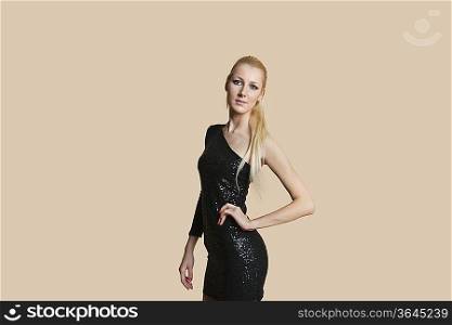 Portrait of a beautiful blond woman wearing cocktail dress with hands on hips over colored background