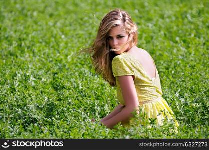 Portrait of a beautiful blonde girl, dressed with a green dress, sitting in a meadow