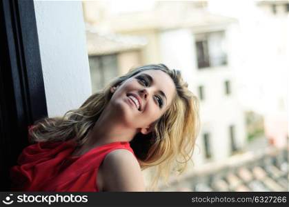 Portrait of a beautiful blonde woman in a window wearing a red dress