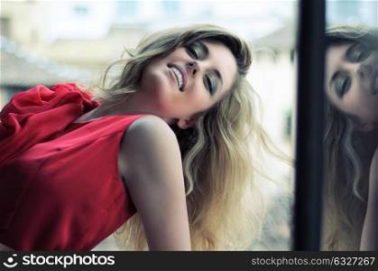 Portrait of a beautiful blonde woman in window wearing a red dress