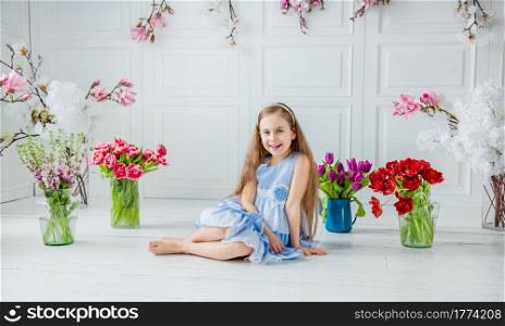 Portrait of a beautiful blue-eyed girl, a little girl among spring flowers in a bright room. Spring break, Mother&rsquo;s Day, Women&rsquo;s Day, Easter.. Portrait of a beautiful blue-eyed girl, a little girl among spring flowers in a bright room.