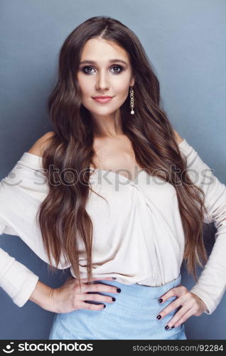 Portrait of a beautiful brunette girl with long wavy hair posing on pastel blue background