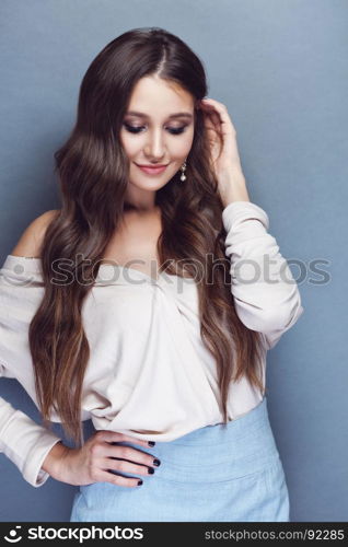 Portrait of a beautiful brunette girl with long wavy hair posing on pastel blue background