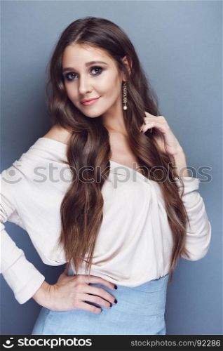 Portrait of a beautiful brunette girl with long wavy hair posing on pastel blue background