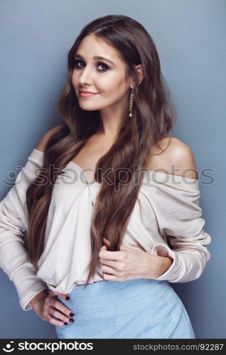 Portrait of a beautiful brunette girl with long wavy hair posing on pastel blue background