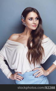 Portrait of a beautiful brunette girl with long wavy hair posing on pastel blue background. There is a gorgeous crystal cuff on her ear.