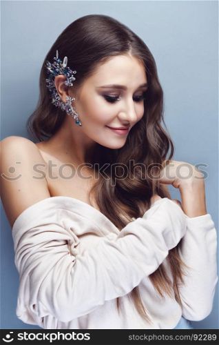 Portrait of a beautiful brunette girl with long wavy hair posing on pastel blue background. There is a gorgeous crystal cuff on her ear.