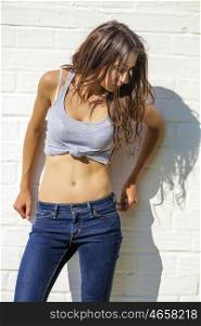 Portrait of a beautiful brunette woman in blue jeans against a white brick wall