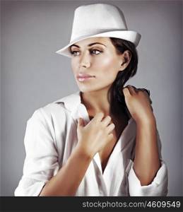 Portrait of a beautiful brunette woman wearing white man's shirt and stylish hat, elegant model posing over gray background, fashion look