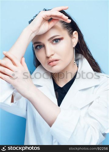 Portrait of a beautiful brunette woman with long hair posing on blue background in white coat