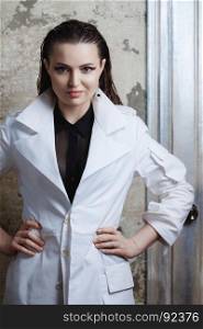 Portrait of a beautiful brunette woman with long hair posing on grunge background in white coat