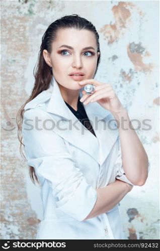 Portrait of a beautiful brunette woman with long hair posing on grunge background in white coat
