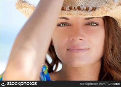 Portrait of a beautiful brunette young woman with stunning green eyes wearing a straw cowboy hat, shot outside in natural light