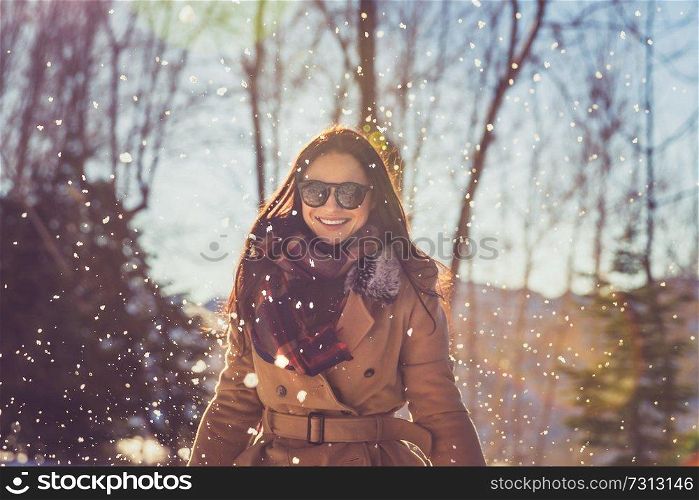 Portrait of a beautiful cheerful female enjoying winter snowfall in the park, with pleasure spending wintertime holidays outdoors