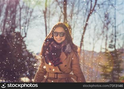 Portrait of a beautiful cheerful female enjoying winter snowfall in the park, with pleasure spending wintertime holidays outdoors