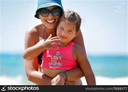 Portrait of a Beautiful Cheerful Mother Hugging her Cute Little Daughter on the Beach. Enjoying Time Together. Happy Summer Vacation.