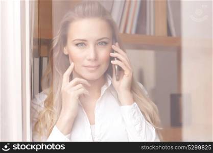 Portrait of a beautiful confident business woman on the phone, standing near windows at the office, young female at work