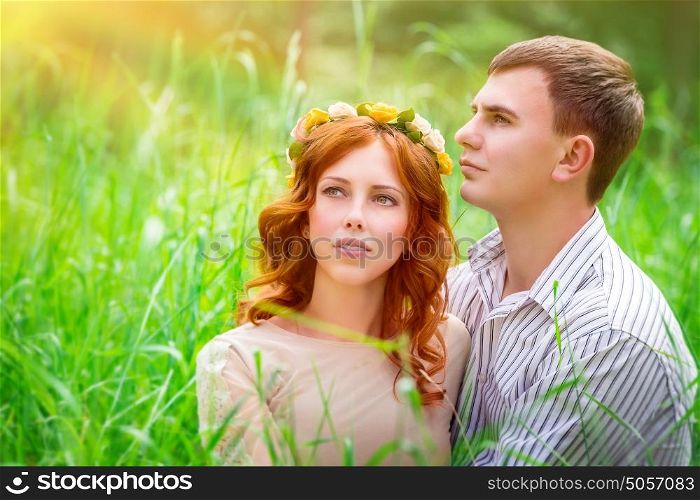Portrait of a beautiful couple sitting in the park on a fresh green grass field and enjoying sunny day, romantic relationship