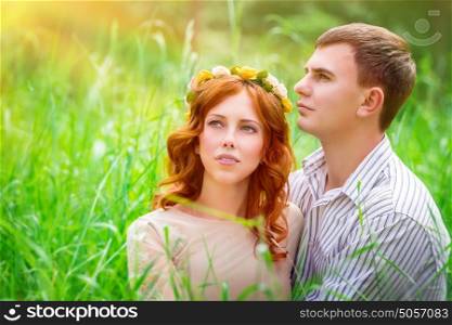 Portrait of a beautiful couple sitting in the park on a fresh green grass field and enjoying sunny day, romantic relationship