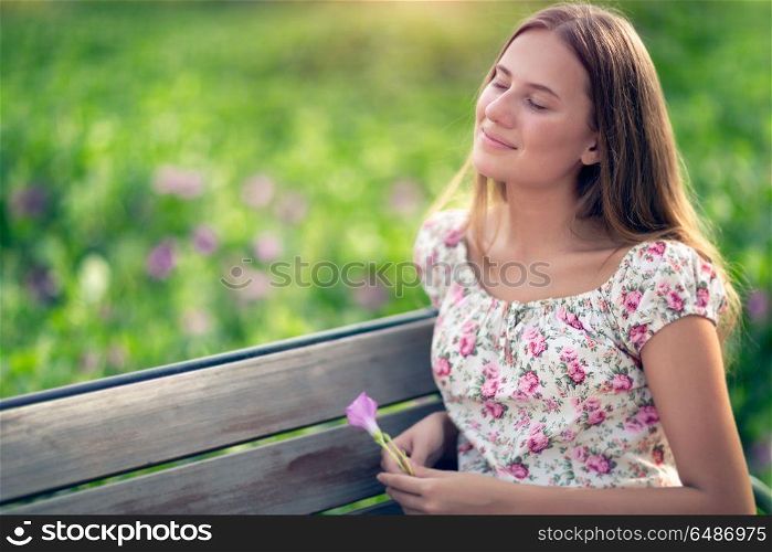 Portrait of a beautiful dreamy student girl sitting on the bench in the park in spring sunny day, closed her eyes with pleasure to feel the warmth of the sun on her face, genuine beauty of youth. Dreamy girl in the park
