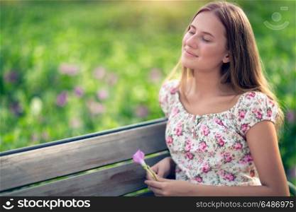 Portrait of a beautiful dreamy student girl sitting on the bench in the park in spring sunny day, closed her eyes with pleasure to feel the warmth of the sun on her face, genuine beauty of youth. Dreamy girl in the park