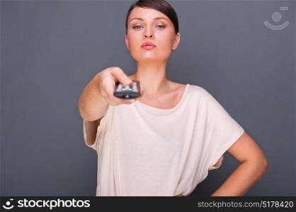 Portrait of a beautiful fashionable elegant woman with remote control choosing channels. Copyspace