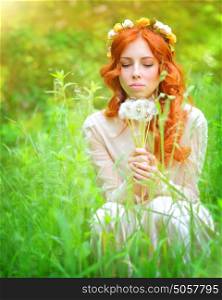 Portrait of a beautiful female wearing floral wreath on red curly hair, enjoying spring garden, holding in hands bouquet of dandelion flowers