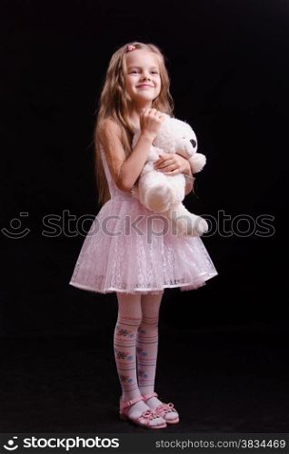 Portrait of a beautiful five year old girl with a teddy bear on a black background