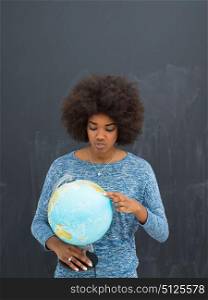 portrait of a beautiful friendly African American woman with a curly afro hairstyle and lovely smile holding Globe of the world isolated on a gray background