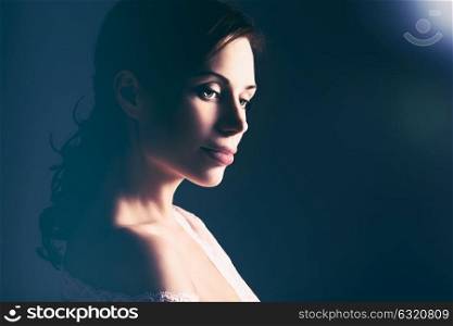Portrait of a beautiful gentle woman in the mild light over dark background, tender elegant bride in the morning, feminine and romantic look