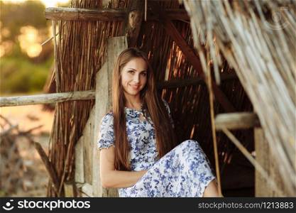 Portrait of a beautiful girl against a wooden house. girl on the background of an old thrown wooden house. girl in white dress with blue embroidery flowers. Portrait of a beautiful girl against a wooden house. girl on the background of an old thrown wooden house. girl in white dress with blue embroidery flowers.