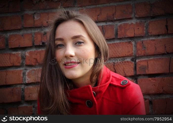 Portrait of a beautiful girl in a red coat on a brick wall background