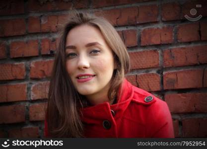 Portrait of a beautiful girl in a red coat on a brick wall background