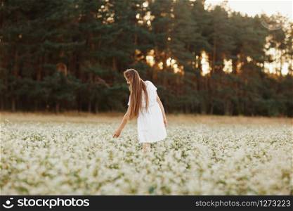 Portrait of a beautiful girl in a white dress in a flowering field. Portrait of a beautiful girl in a white dress in a flowering field. Field of flowers. Summer. unity with nature.
