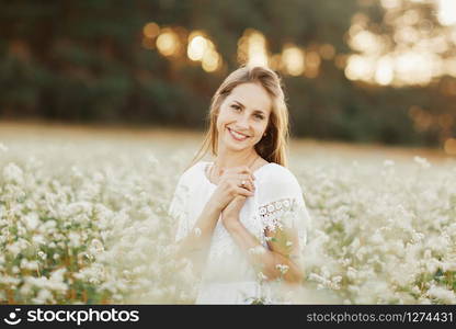 Portrait of a beautiful girl in a white dress in a flowering field. Portrait of a beautiful girl in a white dress in a flowering field. Field of flowers. Summer. unity with nature.