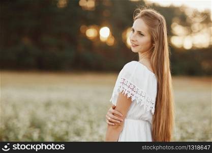 Portrait of a beautiful girl in a white dress in a flowering field. Portrait of a beautiful girl in a white dress in a flowering field. Field of flowers. Summer. unity with nature.