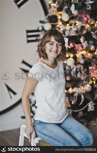 Portrait of a beautiful girl in a white t-shirt on the Christmas tree.. Dream girl thoughtfully sitting by the Christmas tree 7341.
