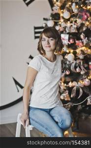 Portrait of a beautiful girl in a white t-shirt on the Christmas tree.. Dream girl thoughtfully sitting by the Christmas tree 7339.