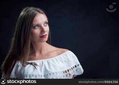 Portrait of a beautiful girl looking up in a loose white dress on a black background