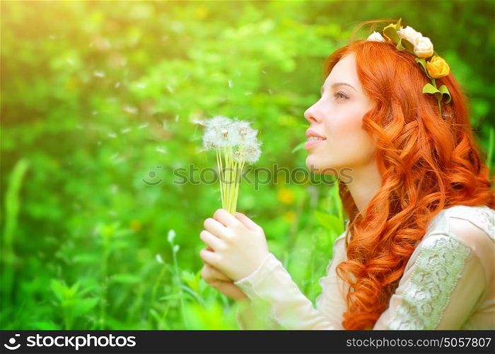Portrait of a beautiful girl wearing floral wreath, enjoying spring grass field, holding in hands bouquet of a dandelion flowers and daydreaming about a wish