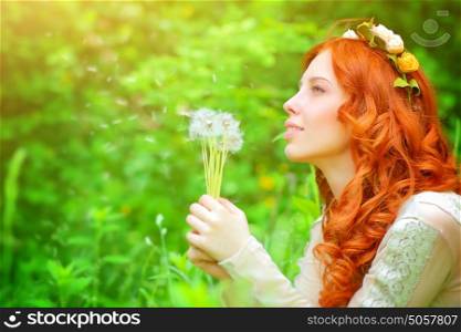 Portrait of a beautiful girl wearing floral wreath, enjoying spring grass field, holding in hands bouquet of a dandelion flowers and daydreaming about a wish