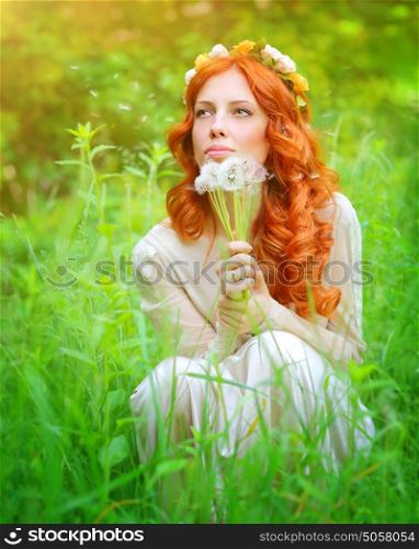 Portrait of a beautiful girl wearing floral wreath on red curly hair, enjoying spring grass field, holding in hands bouquet of dandelion flowers and dreamy making a wish