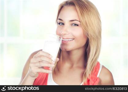 Portrait of a beautiful happy blond woman drinking milk at home, organic beverage for the breakfast, healthy nutrition concept