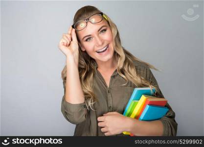 Portrait of a beautiful joyful student girl holding in hands colorful books, isolated on gray background, back to school, enjoying education in the college