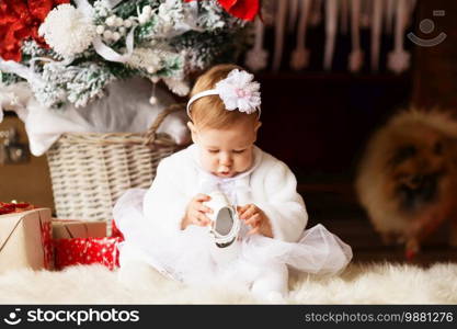 Portrait of a beautiful little girl in a white dress and wrap hair with a flower in the interior with Christmas decorations
