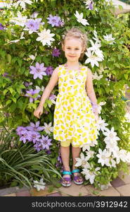 Portrait of a beautiful little girl in summer dress, clematis flowers on background